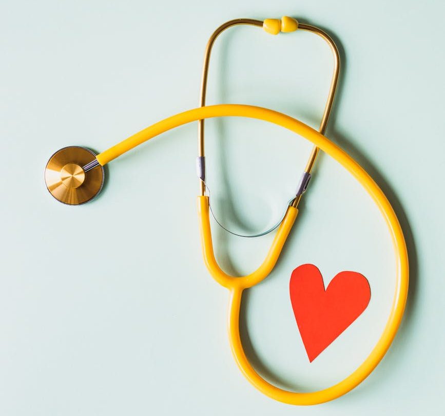 Yellow stethoscope arranged with a red heart cutout on a light green background, symbolizing heart health.