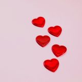 Five red heart shapes on a pastel pink background, ideal for Valentine's Day themes.