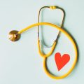 Yellow stethoscope arranged with a red heart cutout on a light green background, symbolizing heart health.