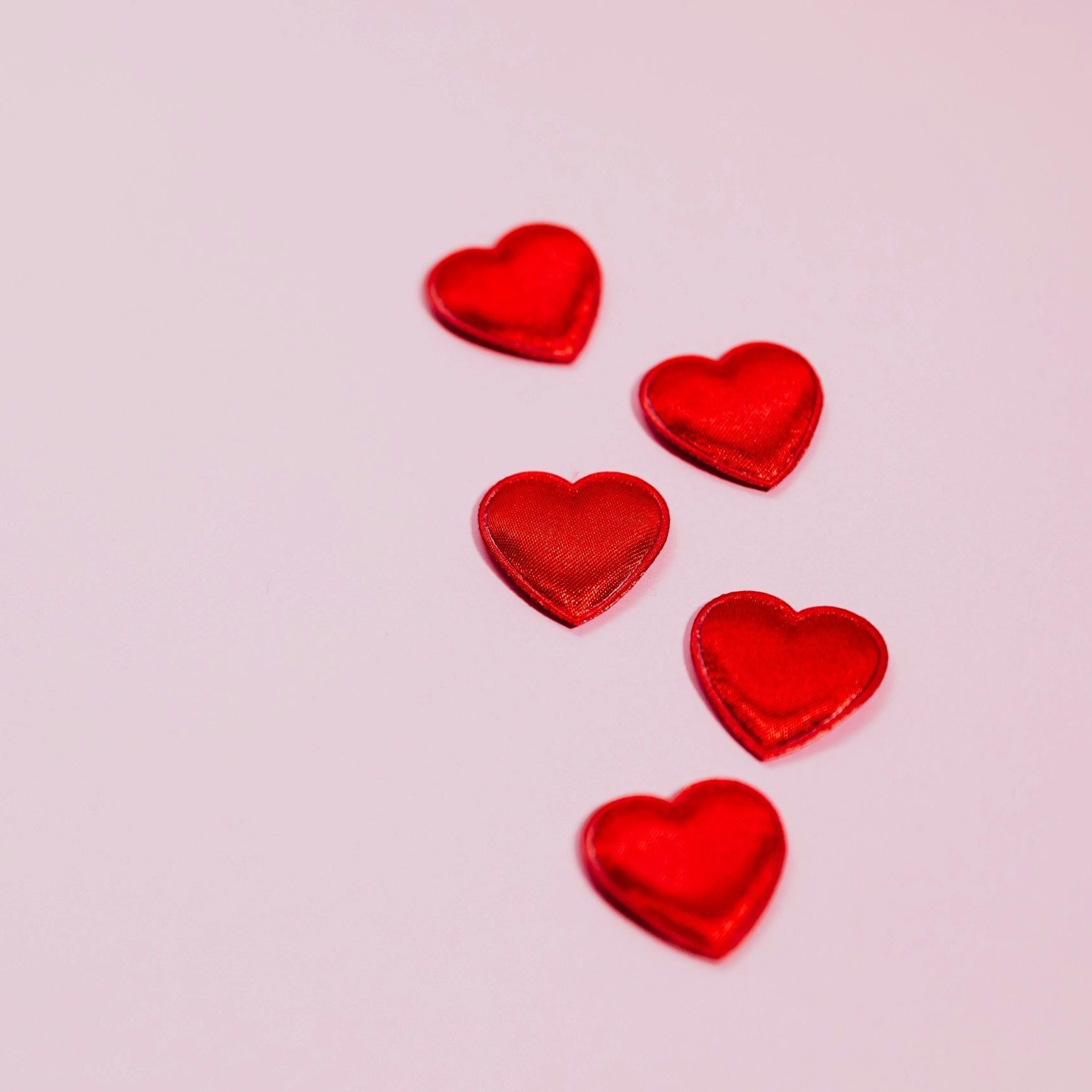 Five red heart shapes on a pastel pink background, ideal for Valentine's Day themes.