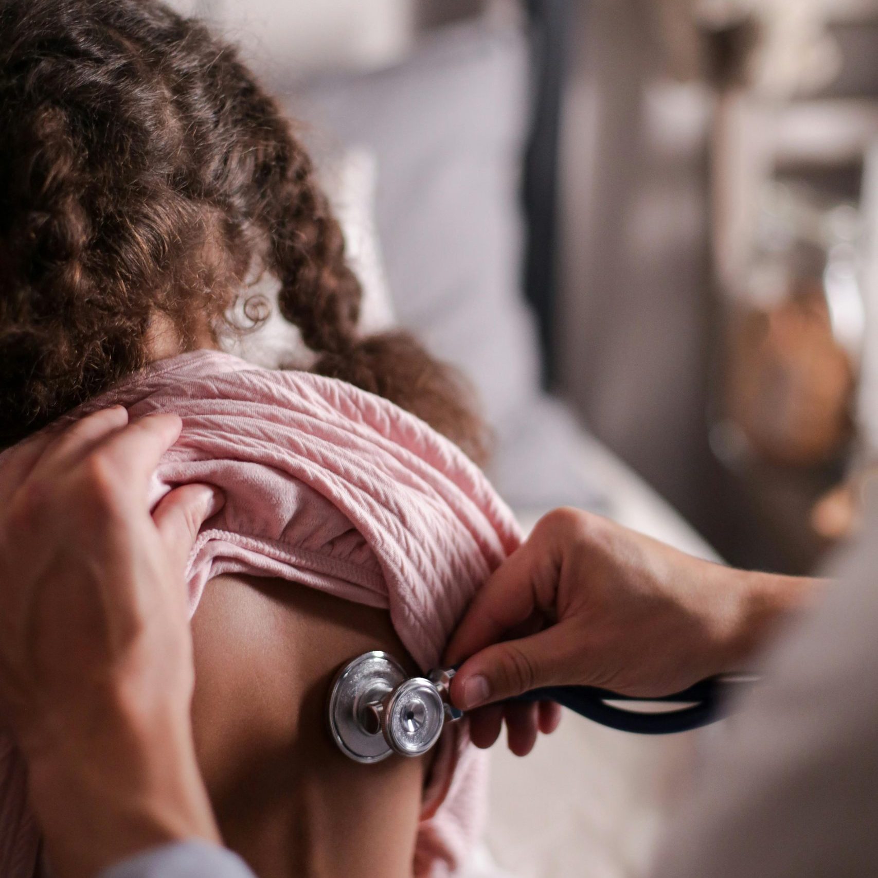 Doctor using stethoscope to check child's back during a health examination indoors.